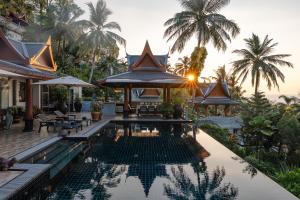 a resort pool with tables and chairs and palm trees at Arun Rapee Villa Surin Beach in Surin Beach
