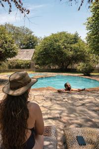 a woman in a hat sitting next to a swimming pool at Thornicroft Lodge - South Luangwa in Mfuwe