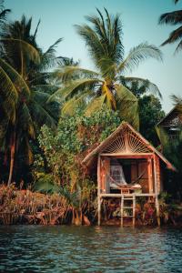 a small hut on the water with palm trees at Eden Eco Village in Kampot