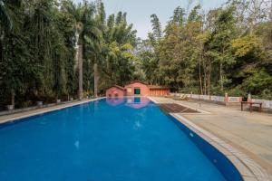 a large blue swimming pool with a house in the background at juSTa The Bagh, Kanha in Bhīmlāt