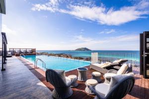 a lounge area with chairs, tables, and a balcony at Aguila Hotel Jeju Oceano Suite in Jeju