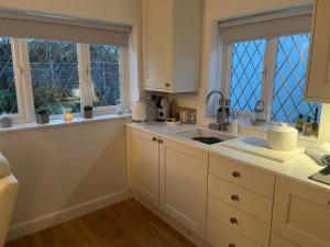 a kitchen with white cabinets and two windows at Garden Lodge, boutique - Walton on Thames in Walton-on-Thames +11 photos
