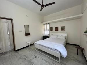a white bedroom with a bed and a ceiling fan at Grey Pearl Homestay in Pondicherry