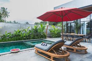a patio with two chairs and an umbrella next to a pool at Pigstone Design Studios Beachfront in Tanah Lot