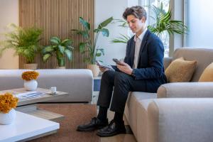 a man in a suit sitting on a couch with a tablet at Hotel SERHS Del Port in Barcelona