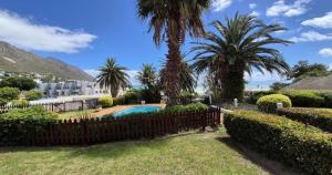 a fence with palm trees and a swimming pool at Beachside Bliss Gordons Bay in Gordonʼs Bay