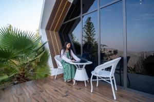 a woman sitting at a table with a laptop on a balcony at SaffronStays Luna Celeste in Rānīkhet