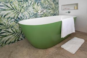 a green bath tub in a bathroom with a tropical wallpaper at Topiary Lux Studio 16! in Herolds Bay +17 photos