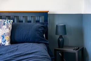 a blue bedroom with a bed with a lamp on a table at Comfy 3 Bed House in Northampton