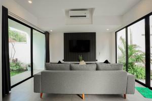 a living room with a gray couch and large windows at Dkenyeri Villa by Aayan in Tanah Lot