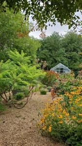 a garden with flowers and a greenhouse in the background at The Oaks Glamping - Rubie's Shepherds Hut in Colkirk