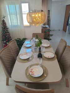 a table with plates and wine glasses and a christmas tree at Quarto próx a Praia do Morro in Guarapari
