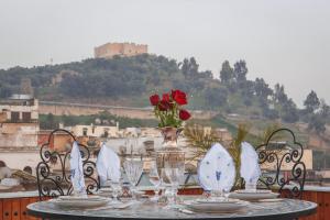 ein Tisch mit Tellern und Gläsern und eine Vase mit Rosen in der Unterkunft Riad Fes Maya suite & spa in Fès