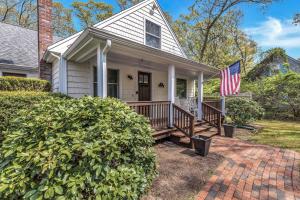 a white house with a porch and an american flag at Jenkins Pond Beach Access with BBall Hoop & Grill, Bright Cape Cod Retreat near Jenkins Pond in Falmouth - Parking, Modern Retreat with Outdoor Space, 24 Hour Hospitality in Falmouth
