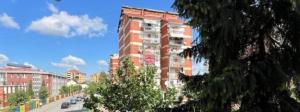a tall building on a city street with cars at Bleon Apartment in Prizren