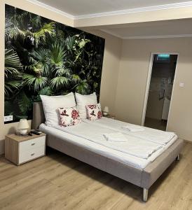 a bed in a room with a wall with plants at Napfény Apartman in Makó
