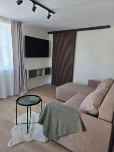 ein Wohnzimmer mit Sofa, Tisch und Fernseher in der Unterkunft Atari Apartment in Ropažu Sala