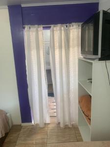 a living room with white curtains and a tv at Pousada Romelandia in Romelândia