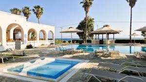 a pool with chairs and umbrellas next to a building at Andromeda Hotel Apartments in Kos