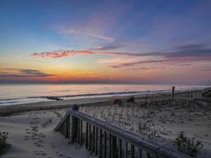 a sunset over the beach with footprints in the sand at Sea Reunion - Nags Head MP 12.5, Oceanfront, Amazing Views! Pool, Hot Tub, Pets OK in Nags Head