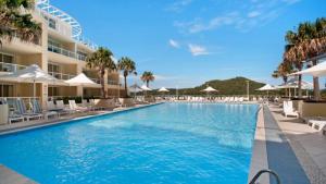 a pool at a resort with chairs and umbrellas at Seashells - Ettalong Beach Resort in Ettalong Beach