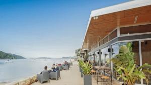 people sitting in chairs on a sidewalk next to the water at Seashells - Ettalong Beach Resort in Ettalong Beach +2 photos