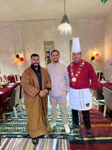 a group of three men standing in a dining room at Camp ainelseid in Kebili