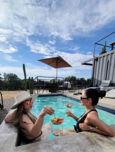 two women sitting next to a swimming pool with drinks at Valle 20 Villa Moderna con Alberca Privada Mayores 12 años in San Antonio de las Minas