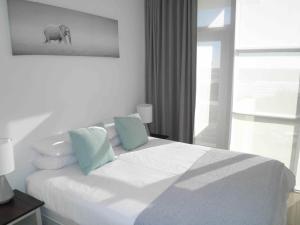 biała sypialnia z łóżkiem z niebieskimi poduszkami w obiekcie 308 St Tropez w mieście Strand