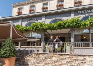 two people standing outside of a restaurant building at Logis hotels Les Glycines in Melle