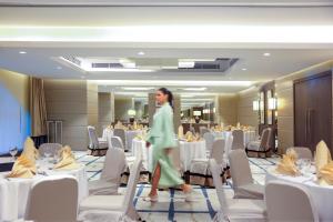 a woman walking through a room with tables and chairs at Al Maha Arjaan by Rotana in Abu Dhabi +104 photos