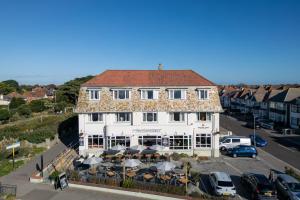 ein weißes Gebäude mit Tischen und Sonnenschirmen auf einem Parkplatz in der Unterkunft Commodore Hotel by Greene King Inns in Bournemouth