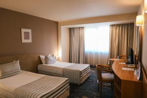 ein Hotelzimmer mit zwei Betten, einem Schreibtisch und einem Fernseher in der Unterkunft Triada Hotel in Sofia + 70 Fotos