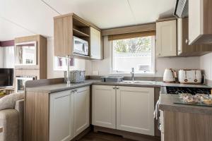 a small kitchen with white cabinets and a sink at Hotel du Van - Rockley Park Caravan, Activities On-site in Poole