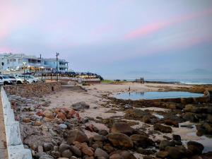 a beach with some rocks and buildings and the ocean at Lilla-Bett Self Catering Mossel Bay in Mossel Bay