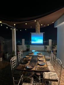 a long wooden table with chairs and a large screen at Adrenalin Surf House in Tamraght Ouzdar