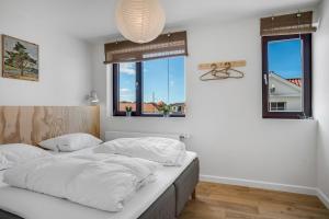 a bedroom with a bed with white sheets and windows at God Plads Og God Beliggenhed I Løkkenshus in Løkken