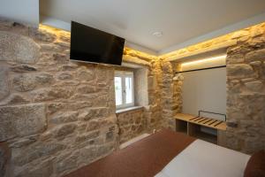a bedroom with a stone wall with a tv on the wall at HOTEL CORONA DE PADRÓN in Padrón
