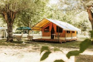a tent with chairs and an umbrella in a field at Camping Onlycamp Les Peupliers in Lepin-le-Lac