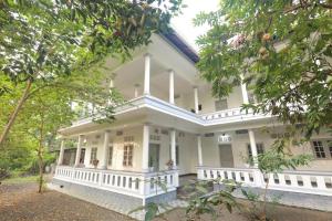 a large white house with trees in the foreground at Greenhaven Homestay Villa in Ettumānūr