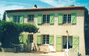 a house with green shutters and a table and chairs at Gîte dans les vignes la calade in Grimaud