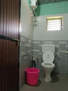 a bathroom with a toilet and a pink bucket at Sheshatara Homestay in Honāvar