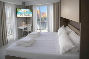 a bedroom with a large white bed and a television at Hotel SoleMare in Diano Marina