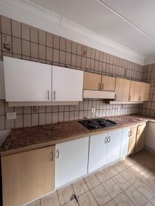 a kitchen with white cabinets and a tile wall at L-PACK PRIMROSe in Germiston