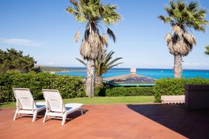 two white chairs sitting on a brick patio with palm trees at Rocca Ruja Vip in Stintino +39 photos