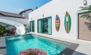 a swimming pool next to a house with a surfboard at Beloved Bliss Pool Villa Bangsaen พูลวิลล่าบางแสนมีสไลด์เดอร์ in Chon Buri