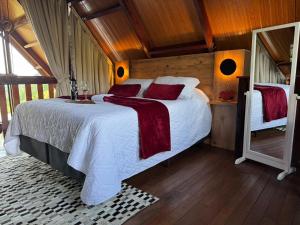 a bedroom with a large bed with white sheets and red pillows at Chalé Mirante dos Anjos in Rodeio