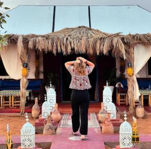 a woman performing a yoga pose in front of a thatch roof at Merzouga Dream Camp in Merzouga