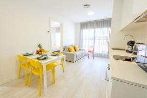 a kitchen and living room with a table and yellow chairs at Castell Beach Aparthotel in Castelldefels