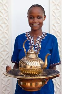 una mujer sosteniendo una tetera dorada en un plato en Kisiwa House, en Zanzíbar